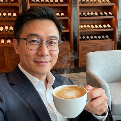 一位戴着眼镜、神情温和的常旅客王先生的半身照，他手持一杯咖啡，身处酒店行政酒廊的休息区。